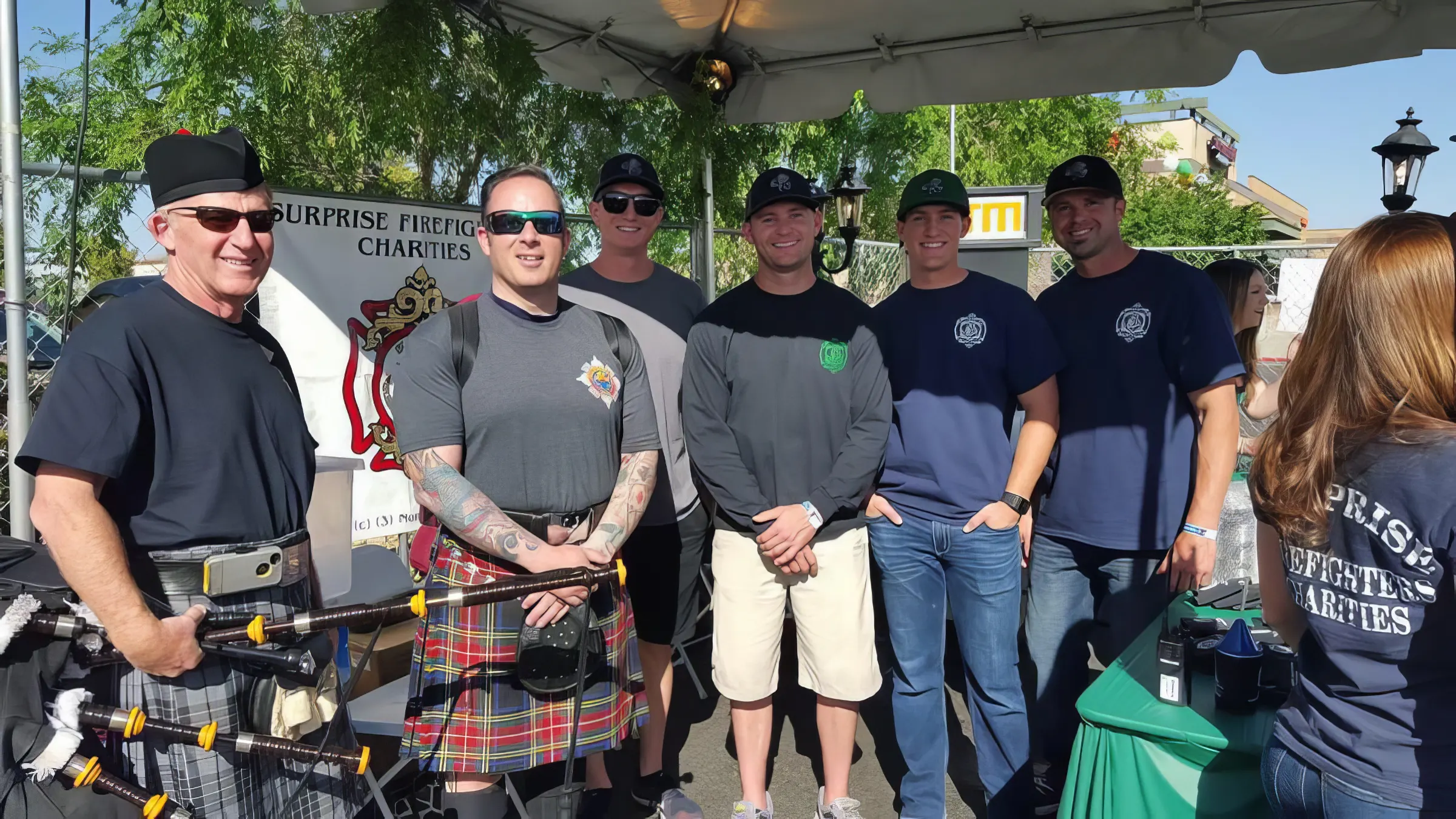 Crews and the pipe band under the Surprise Firefighters Charities tent at a community event.
